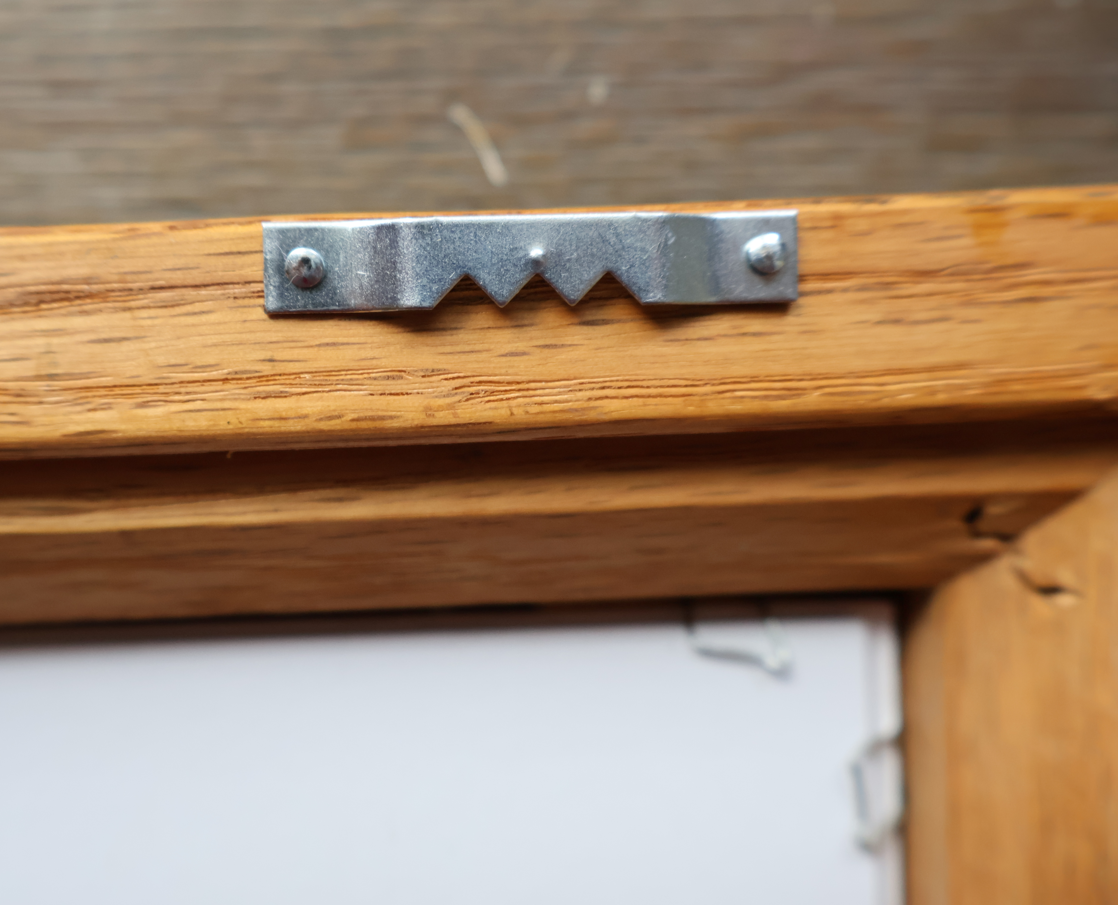 A close-up of a silver metal mounting bracket with a zigzag cutout, secured with two screws onto a wooden frame.