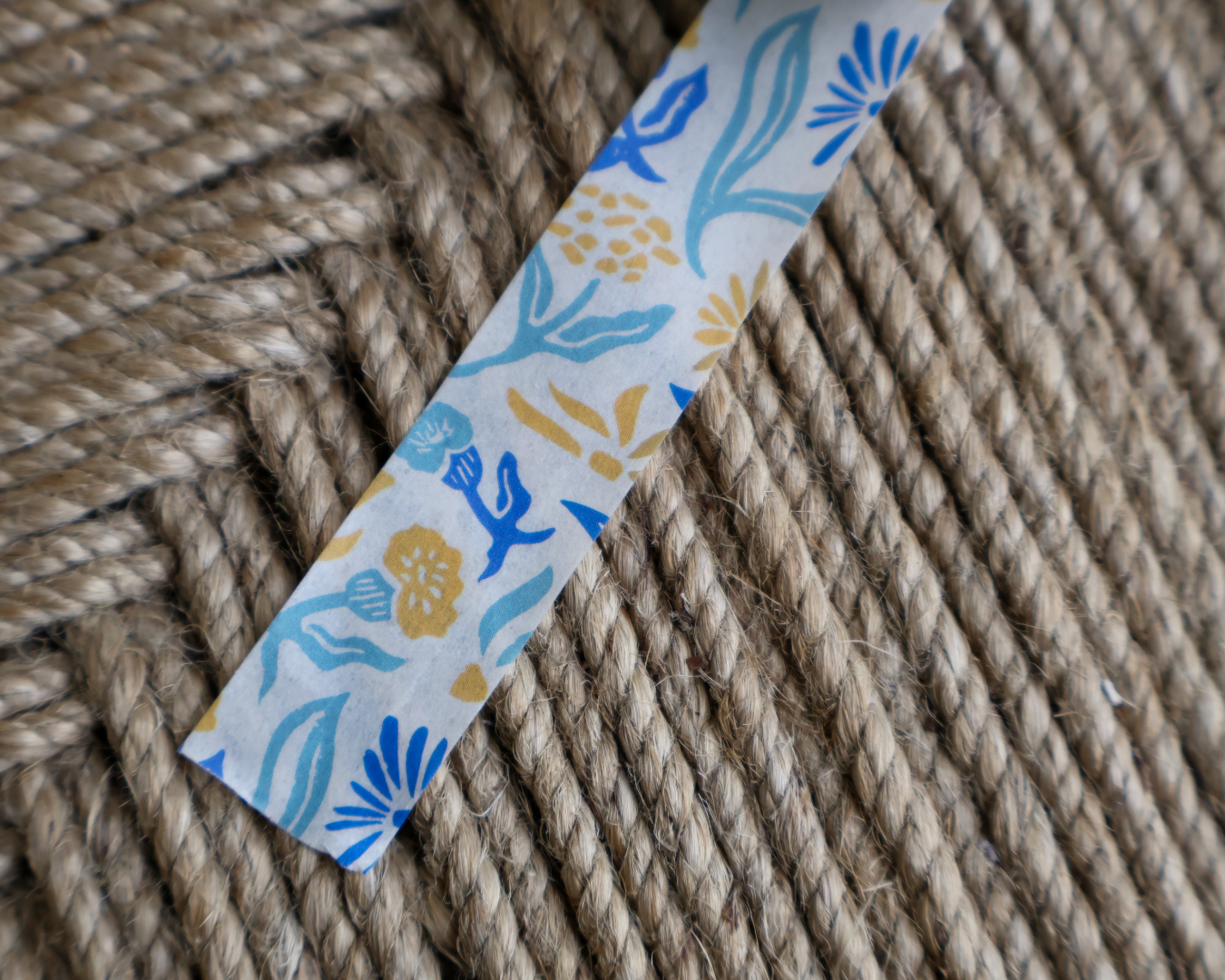 linocut design of blue, gold, and cream organic flowers on decorative washi tape. unrolled showing the design on a textured brown background. by dovetail studio