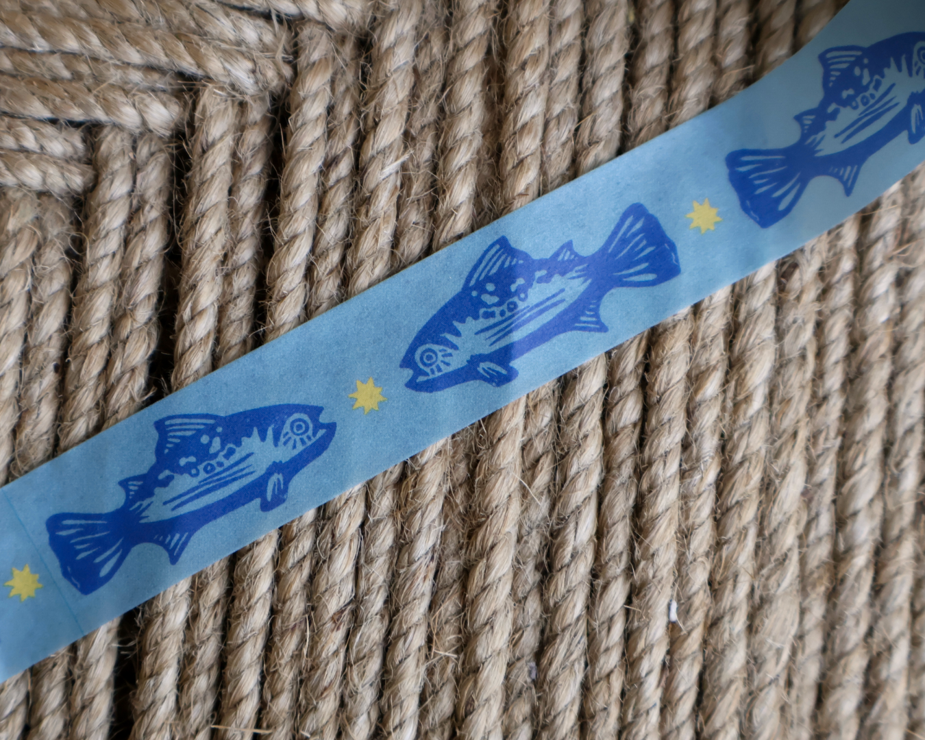 linocut design of blue trout fish with gold star on decorative washi tape. unrolled showing the design on a textured brown background. by dovetail studio