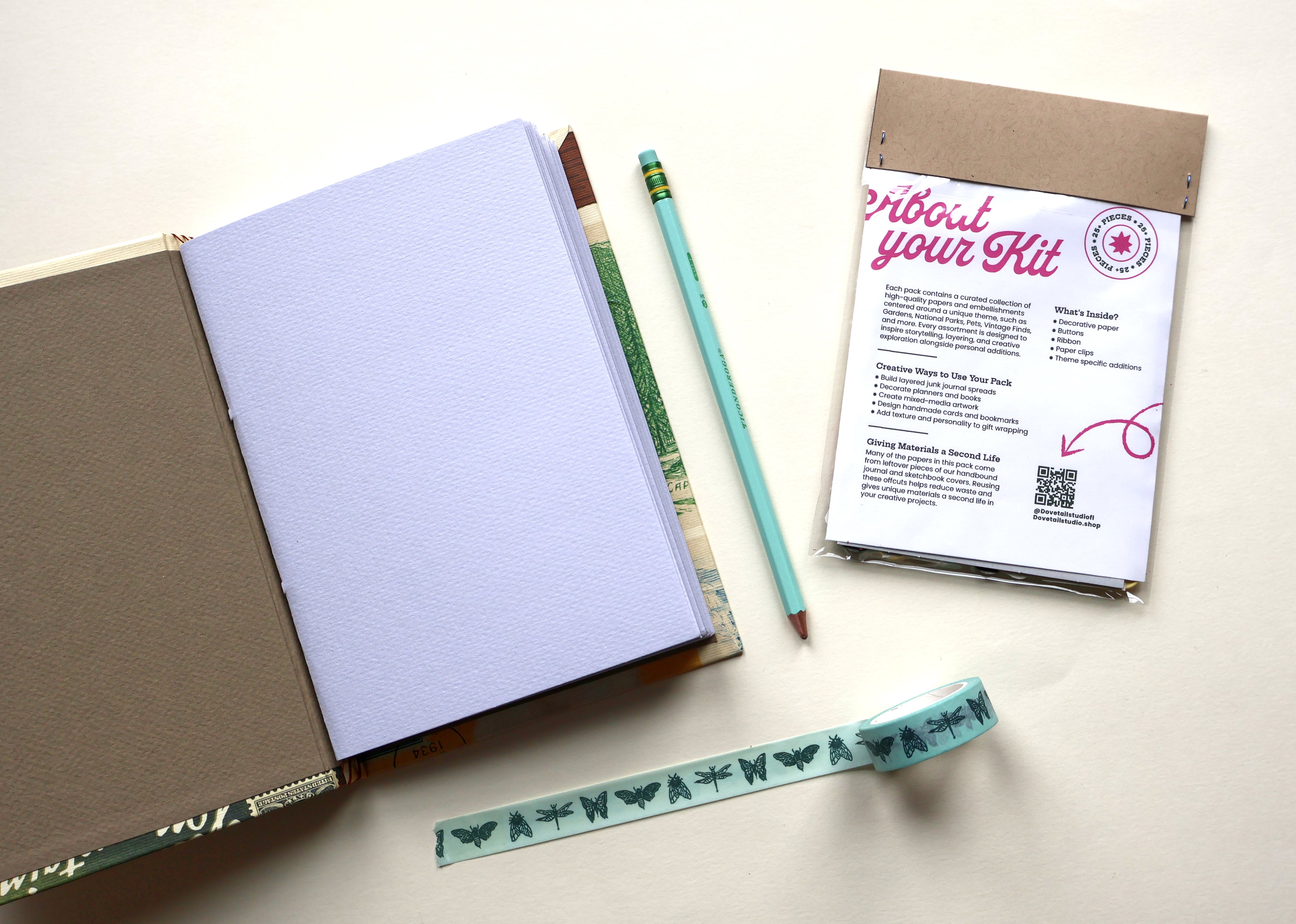 An open sketchbook with blank paper pages, a mint green pencil, a kraft envelope containing a printed kit card, and a decorative insect washi tape strip with butterfly and dragonfly motifs, arranged on a light beige surface.