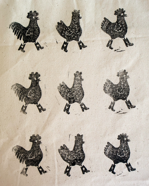 closeup of the pattern showing chickens walking in boots on a cotton totebag. handmade linocut print black on canvas