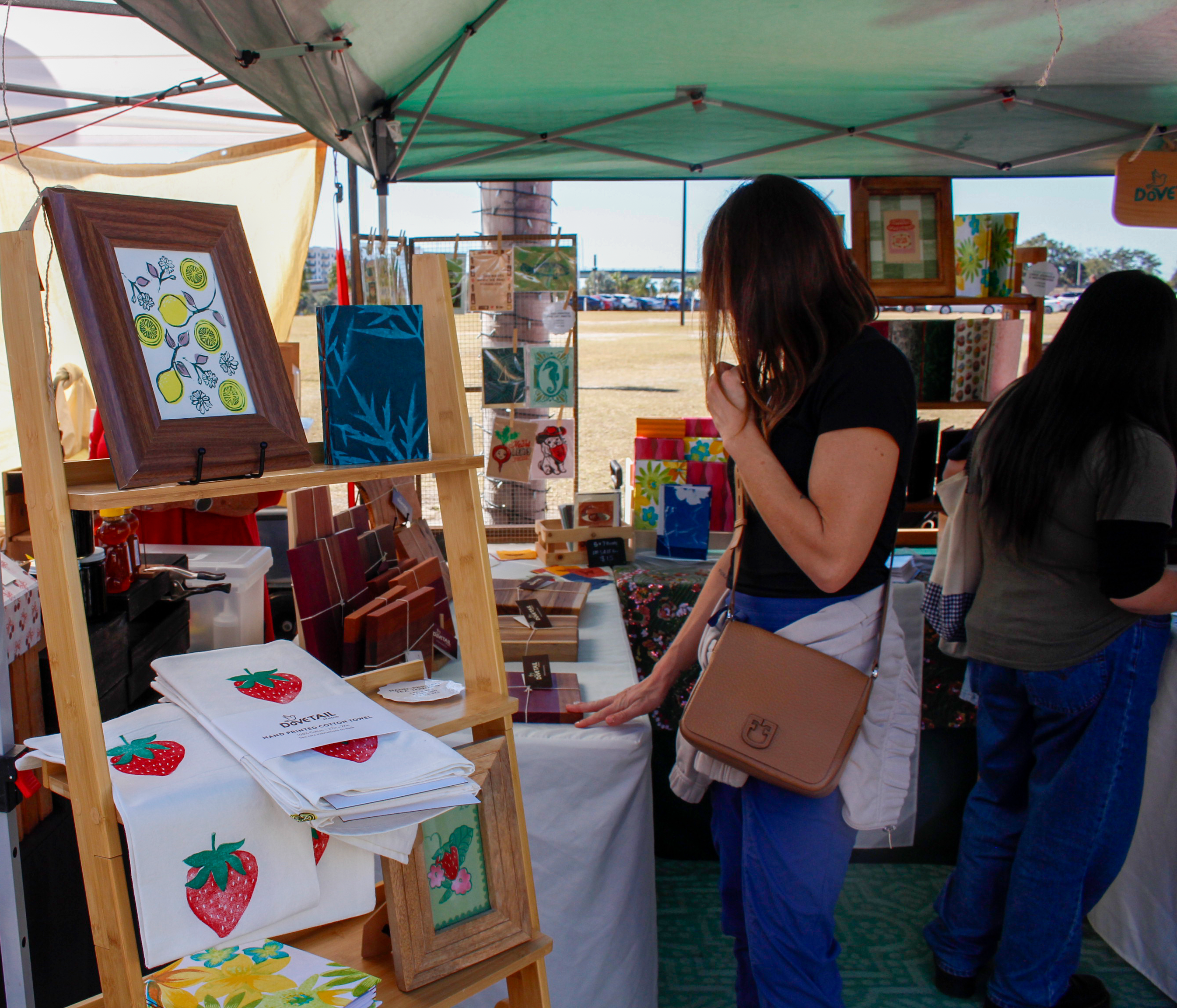 Artisanal Dovetail Studio booth with artwork such as handprinted linocut goods, handbound books, and woodworking and a woman looking at items