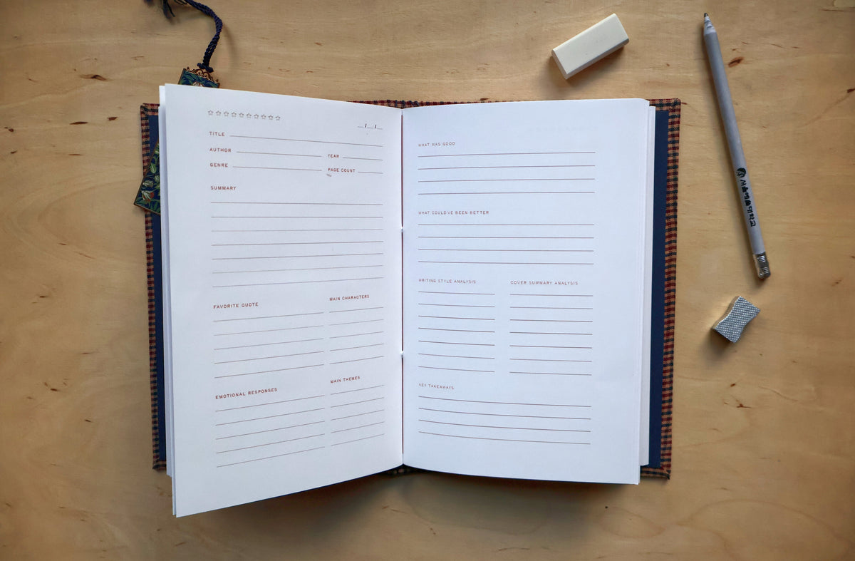 An open reading log with lined pages lies on a light wood tabletop, surrounded by a pencil, erasers, and a small decorative tag.