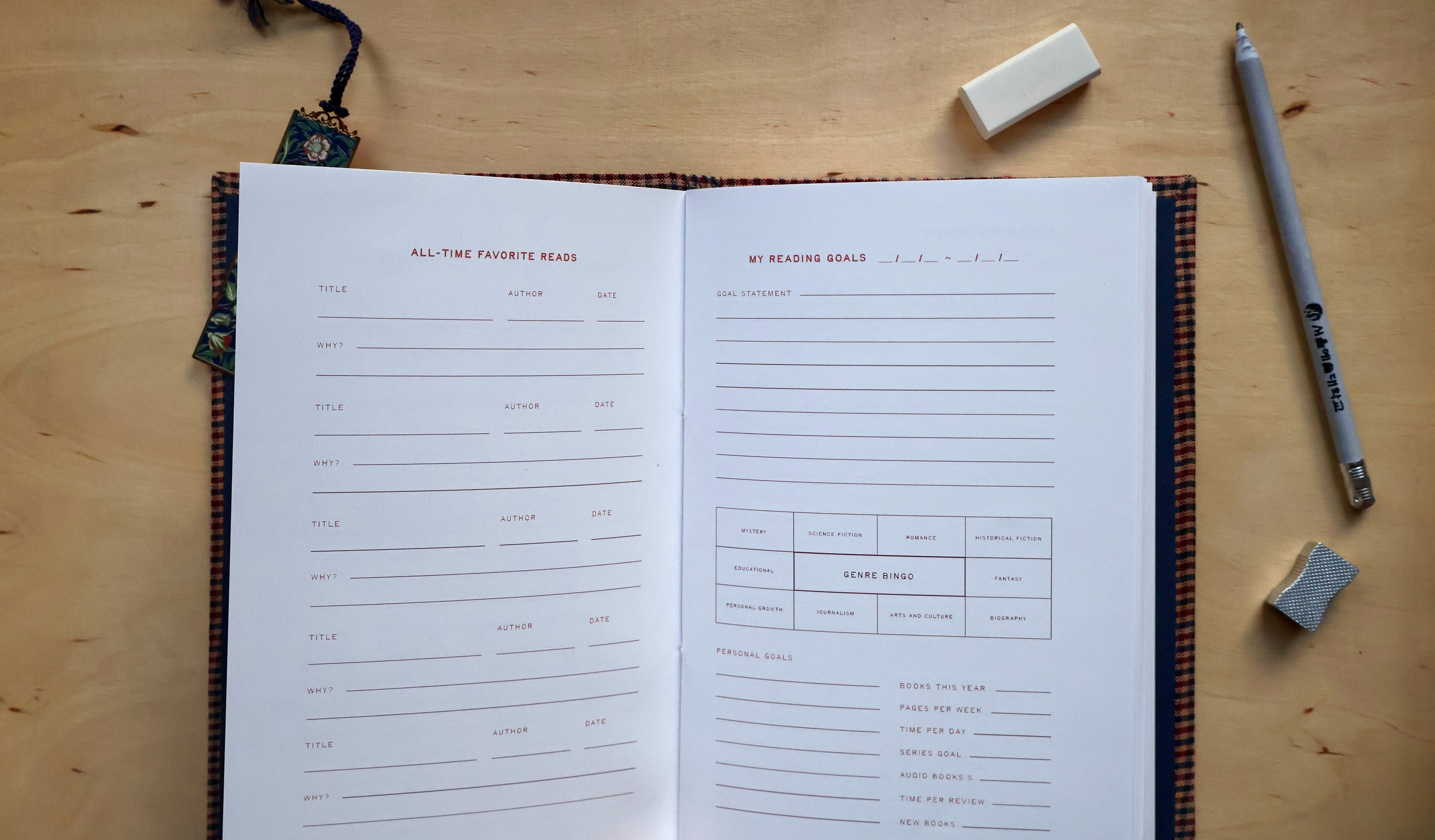An open lined reading log spread on a light wood tabletop, with writing prompts on both pages and surrounding stationery including a pencil, eraser, and small accessory.