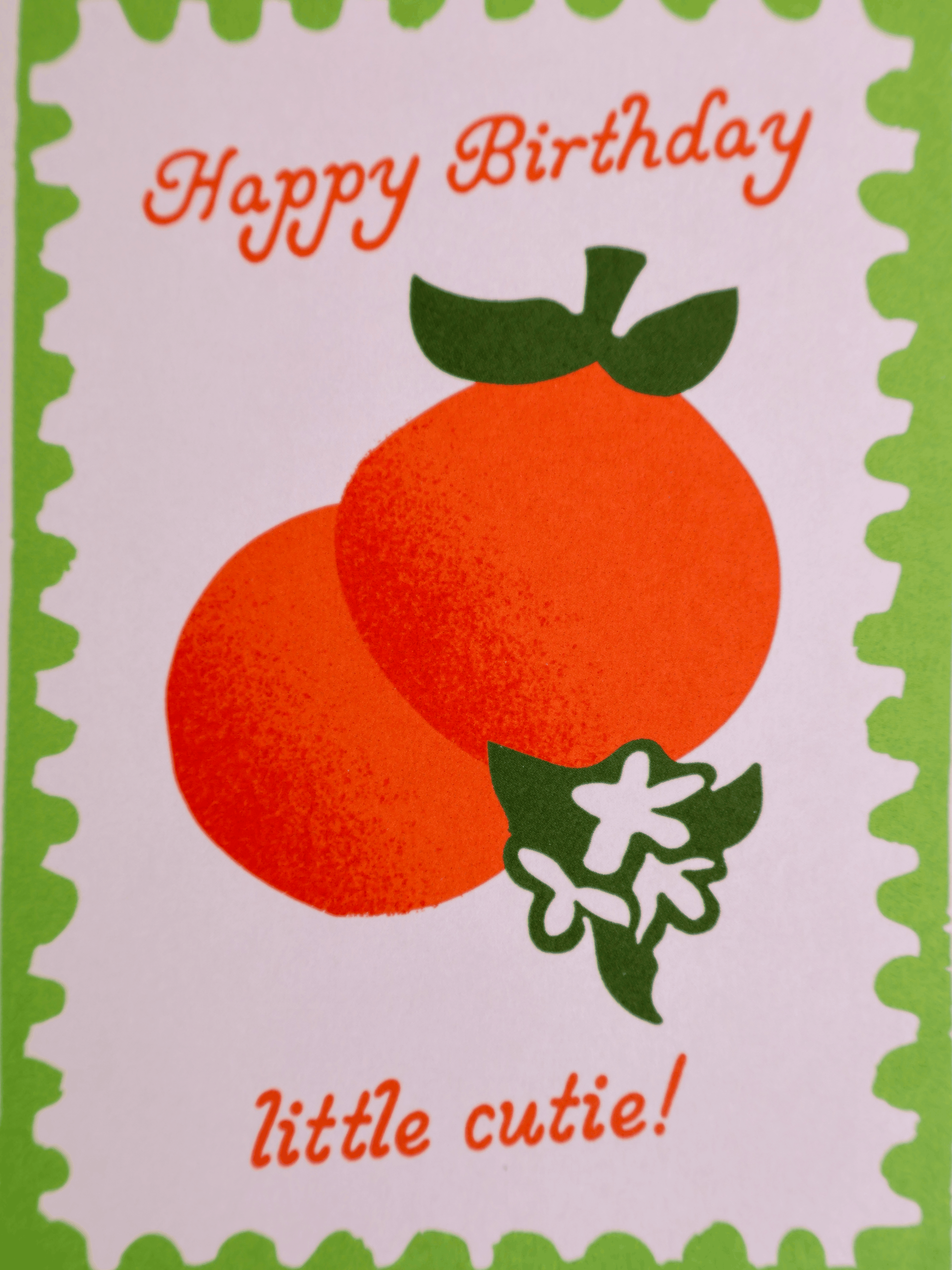 A square greeting card with a scalloped green border, featuring two orange fruits and green leaves on a white background, with the text 'Happy Birthday little cutie!' in orange script.