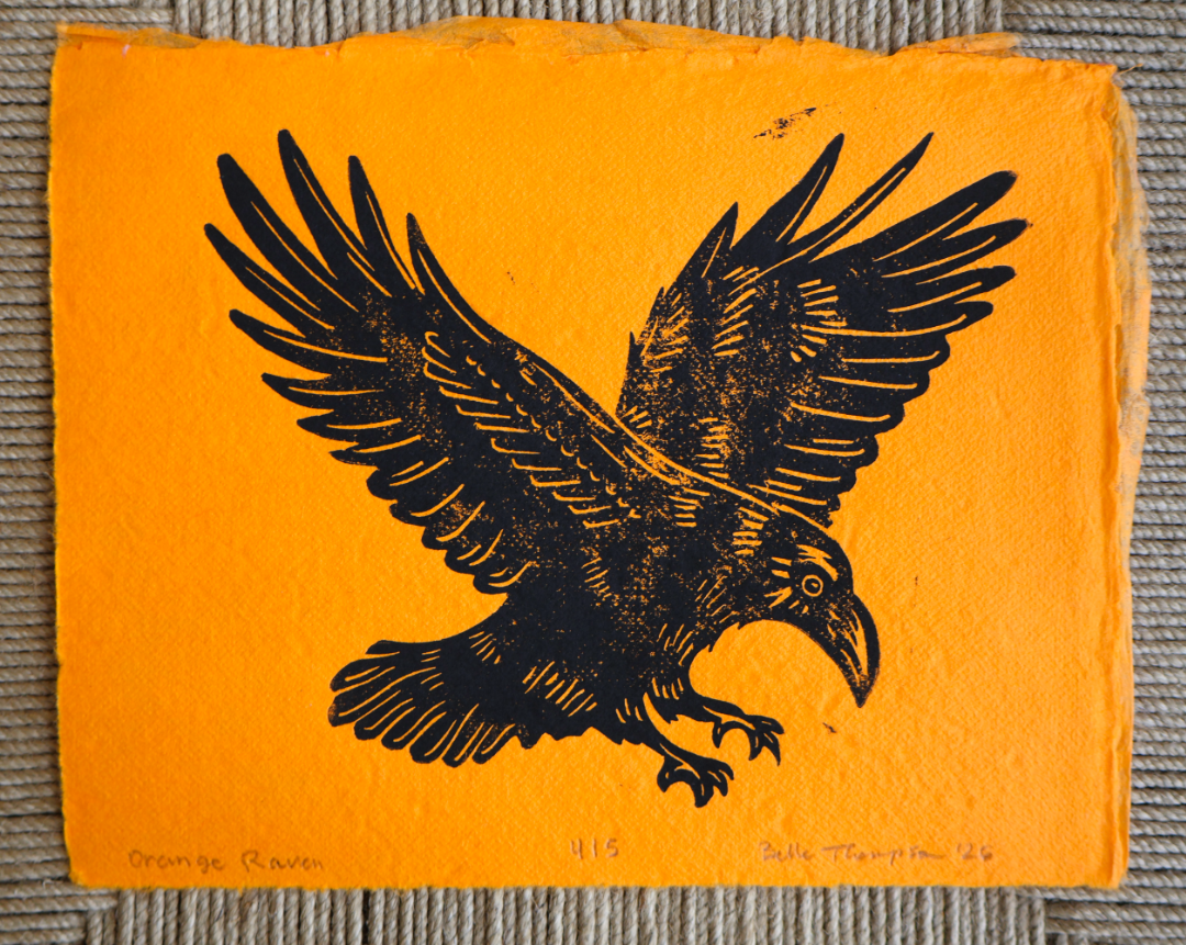 An orange art print or card featuring a black bird of prey illustration, photographed flat against a gray textured fabric background.