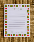 A white notepad with a decorative border of strawberries and sunflowers, titled 'TODAY'S TO-DO HOPEFULLY' and 'FINISHED?', placed on a woven tan surface.