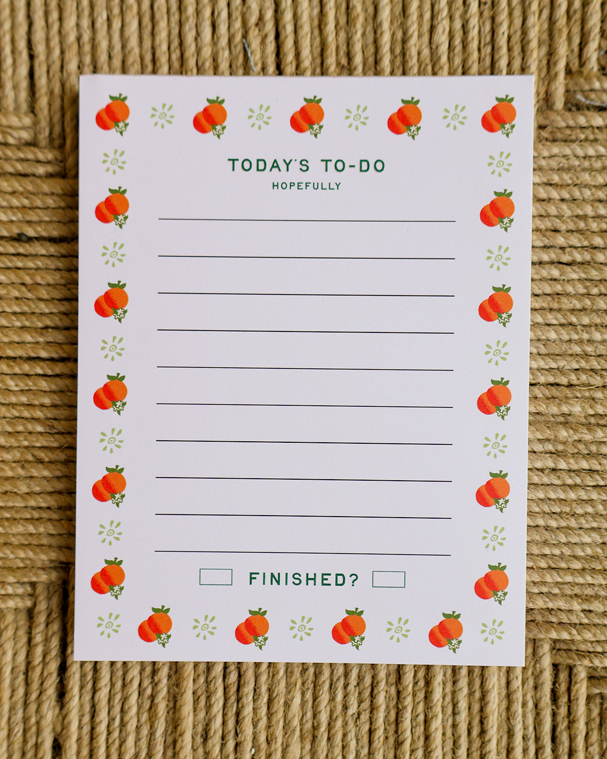 A white notepad with a cute fruit-themed border and 'TODAY'S TO-DO' text, placed flat on a woven jute surface.