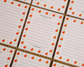 A close-up of a grid of white to-do list cards with a repeating border of oranges and small green leaves, arranged on a brown textured surface. Linocut Design