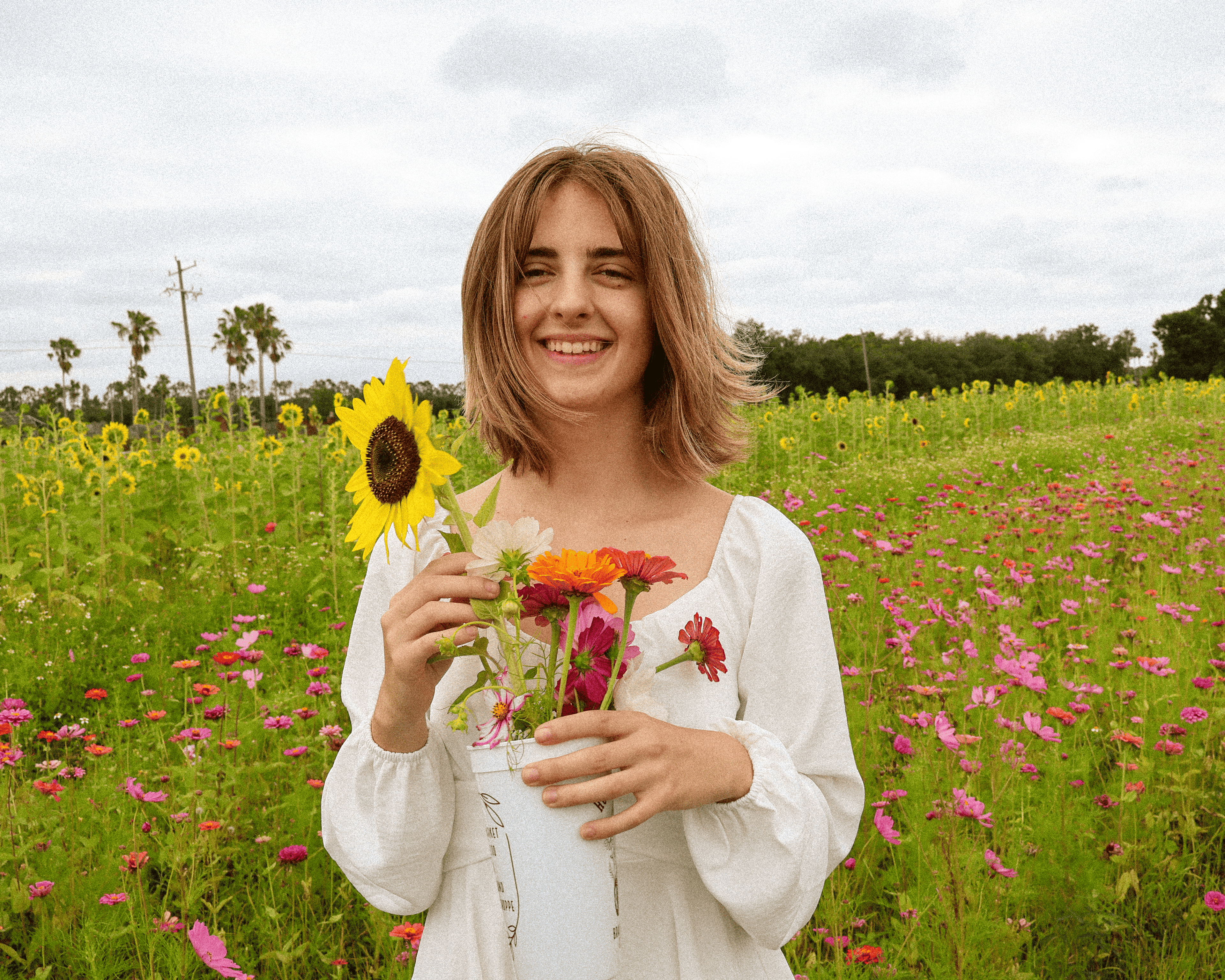 photograph of the prettiest girl in the world bella thompson who is also the co-owner of Dovetail Studio, specializing in linocut printmaking pictured in a field of flowers holding a sunflower