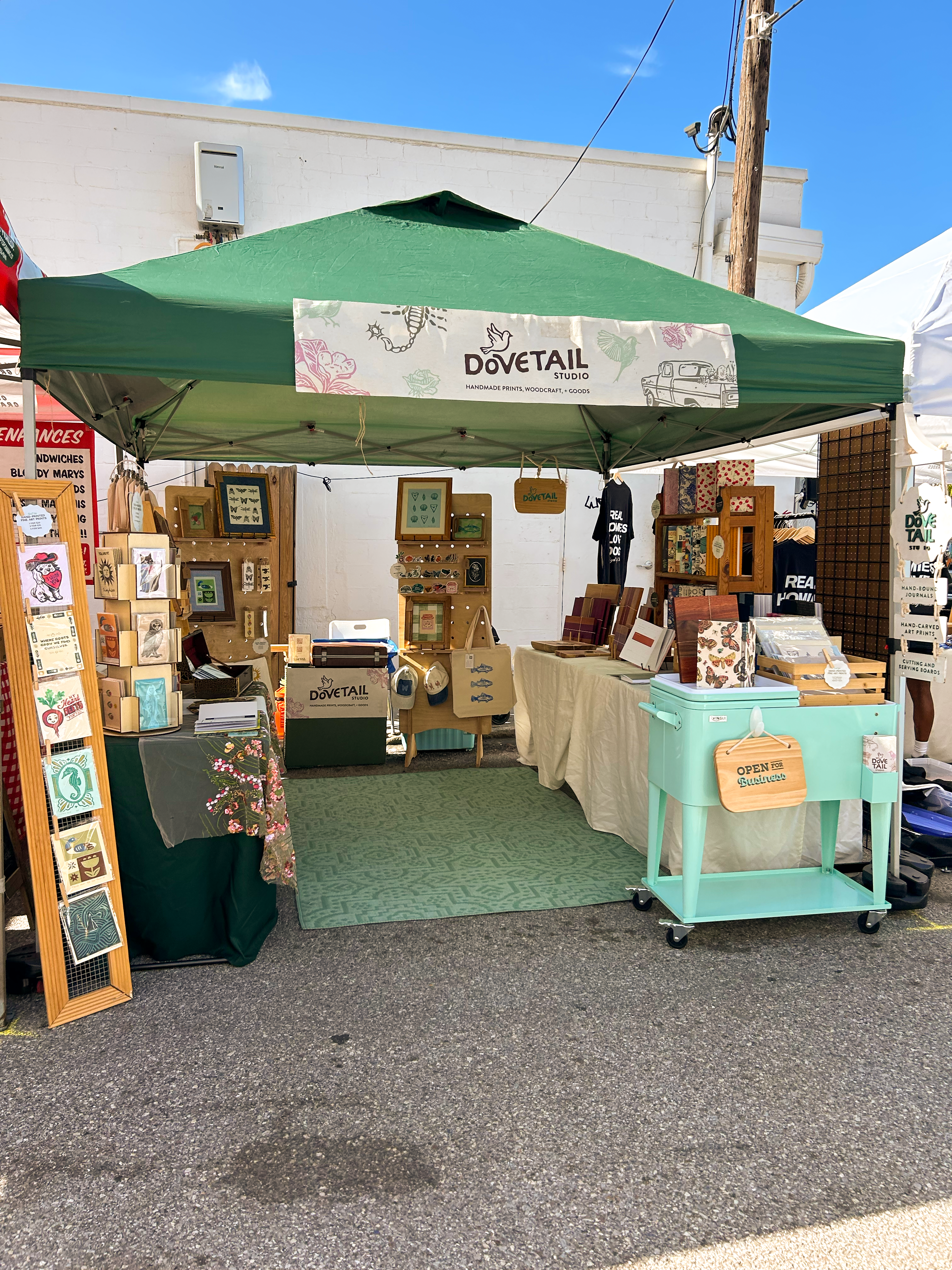outdoor market setup for dovetail studio featuring handmade linocut prints, hand bound journals, stationery, and wood working in st petersburg florida