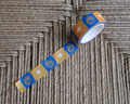 linocut design of checkered blue, gold, and cream organic flowers and star on decorative washi tape. unrolled showing the design on a textured brown background. by dovetail studio