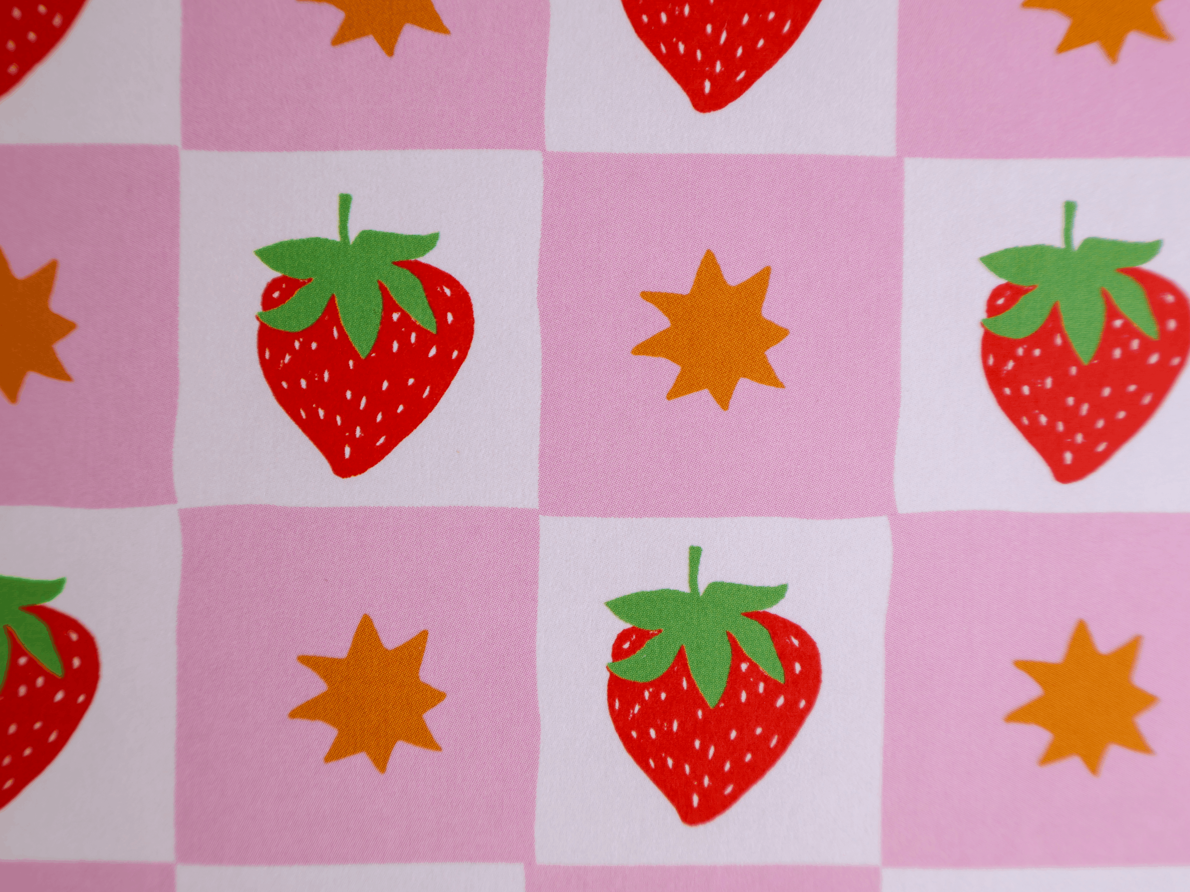 A close-up of a pink and white checkered fabric or wallpaper pattern featuring red strawberries with green leaves and orange starburst motifs.