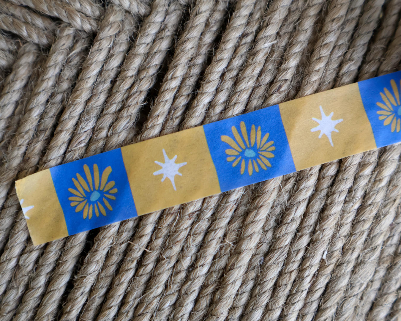 linocut design of checkered blue, gold, and cream organic flowers and star on decorative washi tape. unrolled showing the design on a textured brown background. by dovetail studio