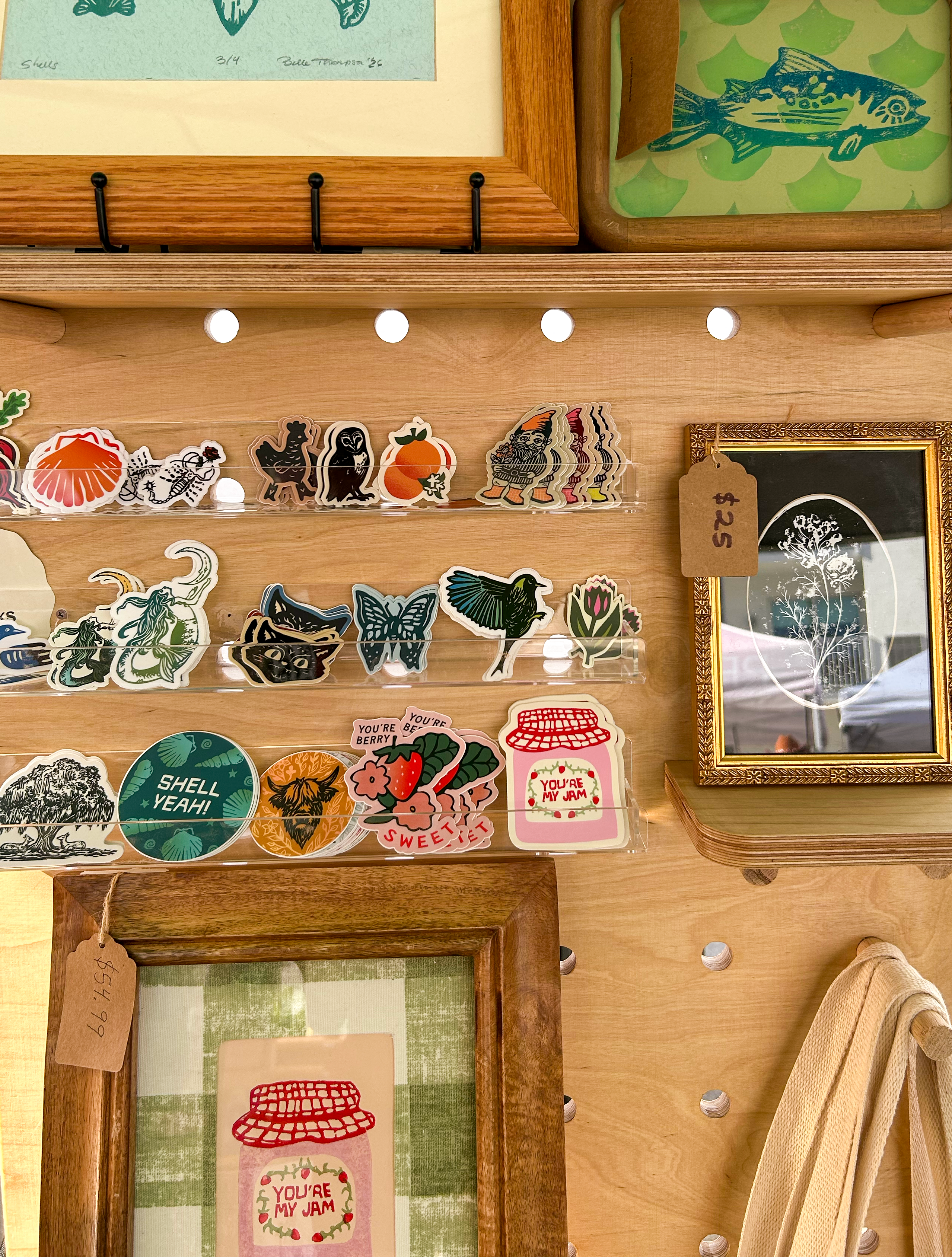framed handmade linocut prints, stickers, and totebags of trout fish, youre my jam strawberry jam, bebys breath flowers, shark teeth, shells, butterflies, birds, garden gnomes, oranges, chickens with boots, scorpions, beets, willow trees, deer, heron, cats, sirens or mermaids, owls, and cows