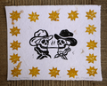A square white art print or card featuring a western-themed design: two black-and-white skulls wearing hats facing each other, surrounded by a border of yellow starbursts, photographed flat against a brown woven surface.