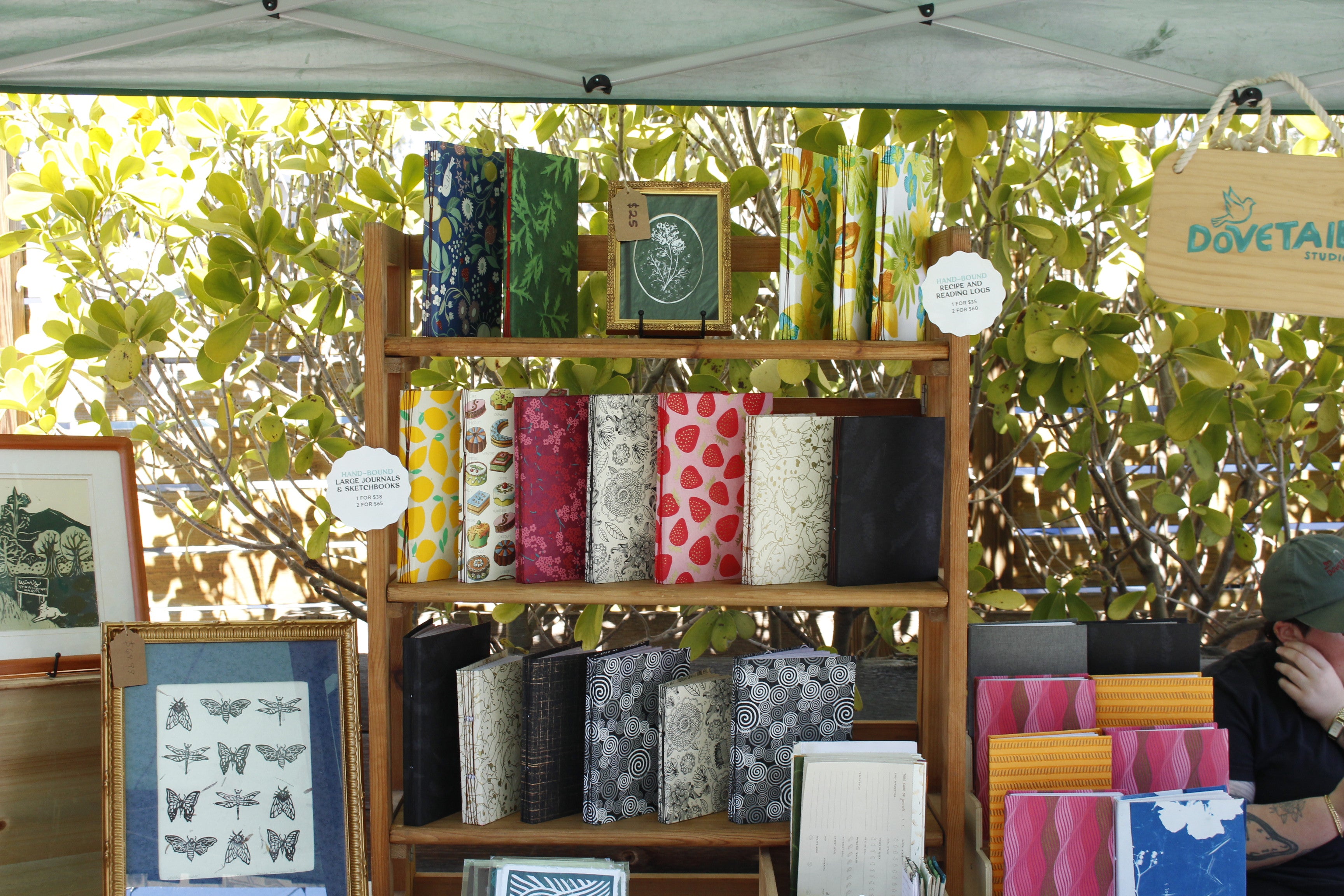 display of colorful handmade journals sketchbooks reading logs recipe logs framed handmade linocut prints stationery with imagery of bugs, flowers, strawberries, and patterns