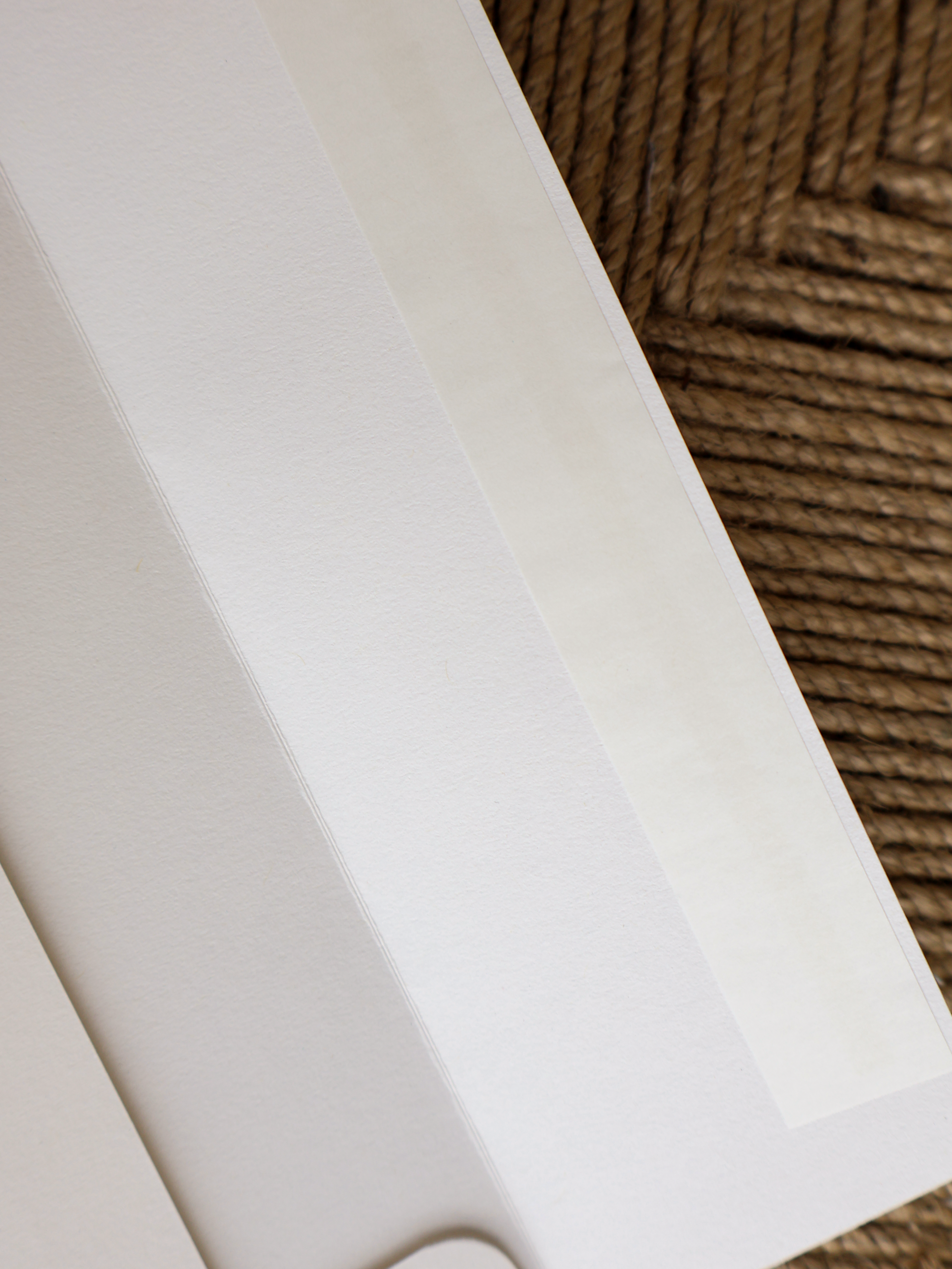 A close-up of a white textured paper sheet or card with a translucent adhesive strip along one edge, placed diagonally on a brown woven rug.