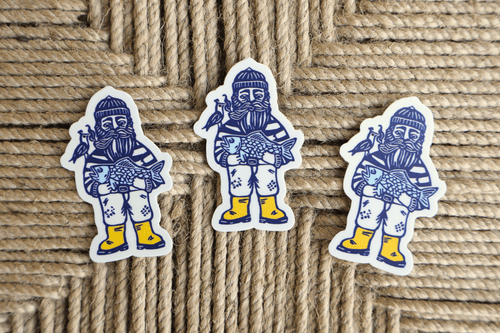 Three die-cut stickers featuring a stylized blue and white fisherman holding a fish, with yellow boots, arranged on a woven jute background.