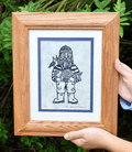 fisherman linocut print in wood frame with green foliage in background
