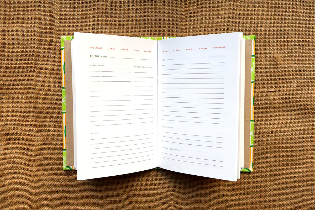An open recipe log with lined pages for planning, displayed on a brown burlap background.
