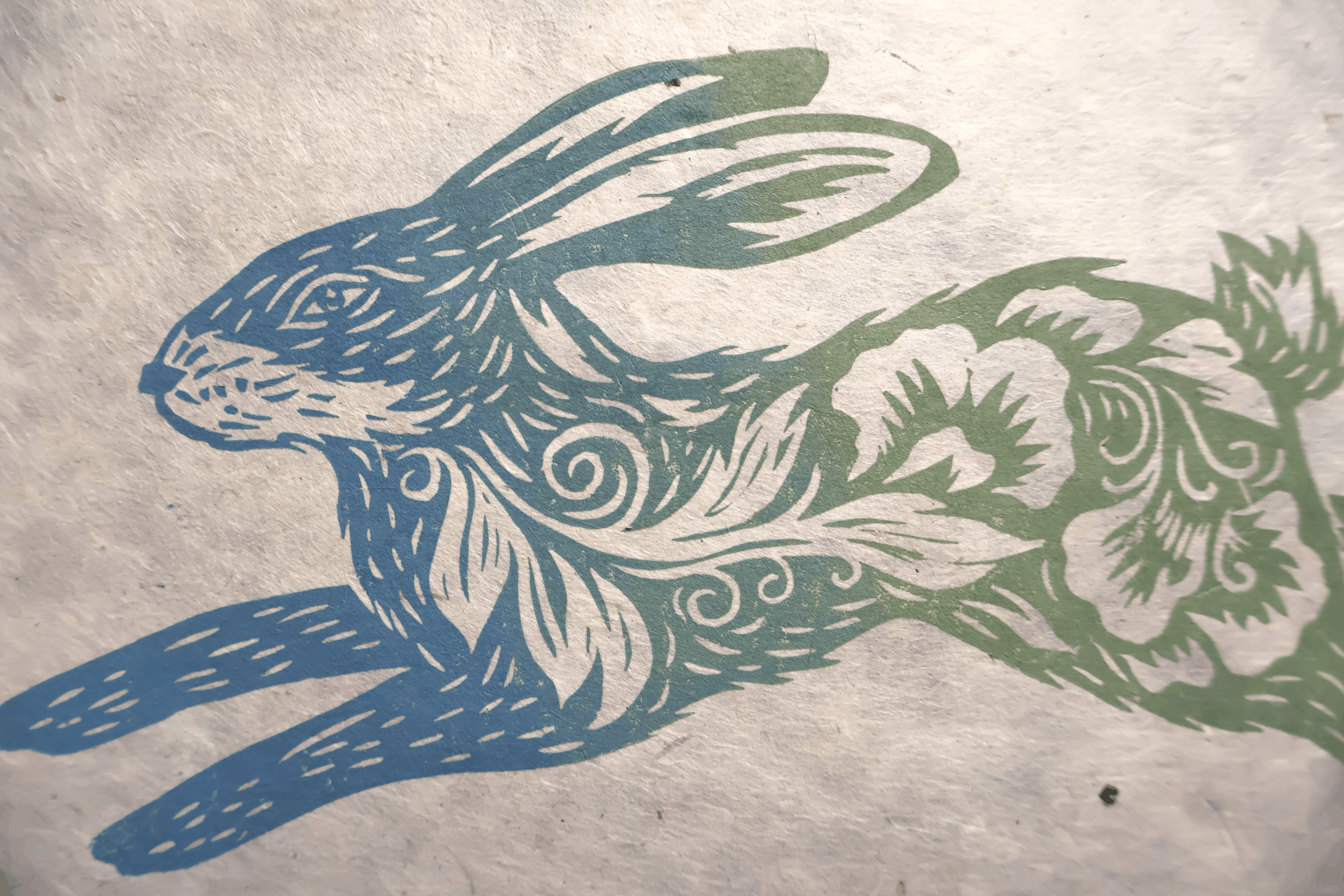 A close-up of a textured paper print featuring a stylized rabbit in blue and green with white carved details.