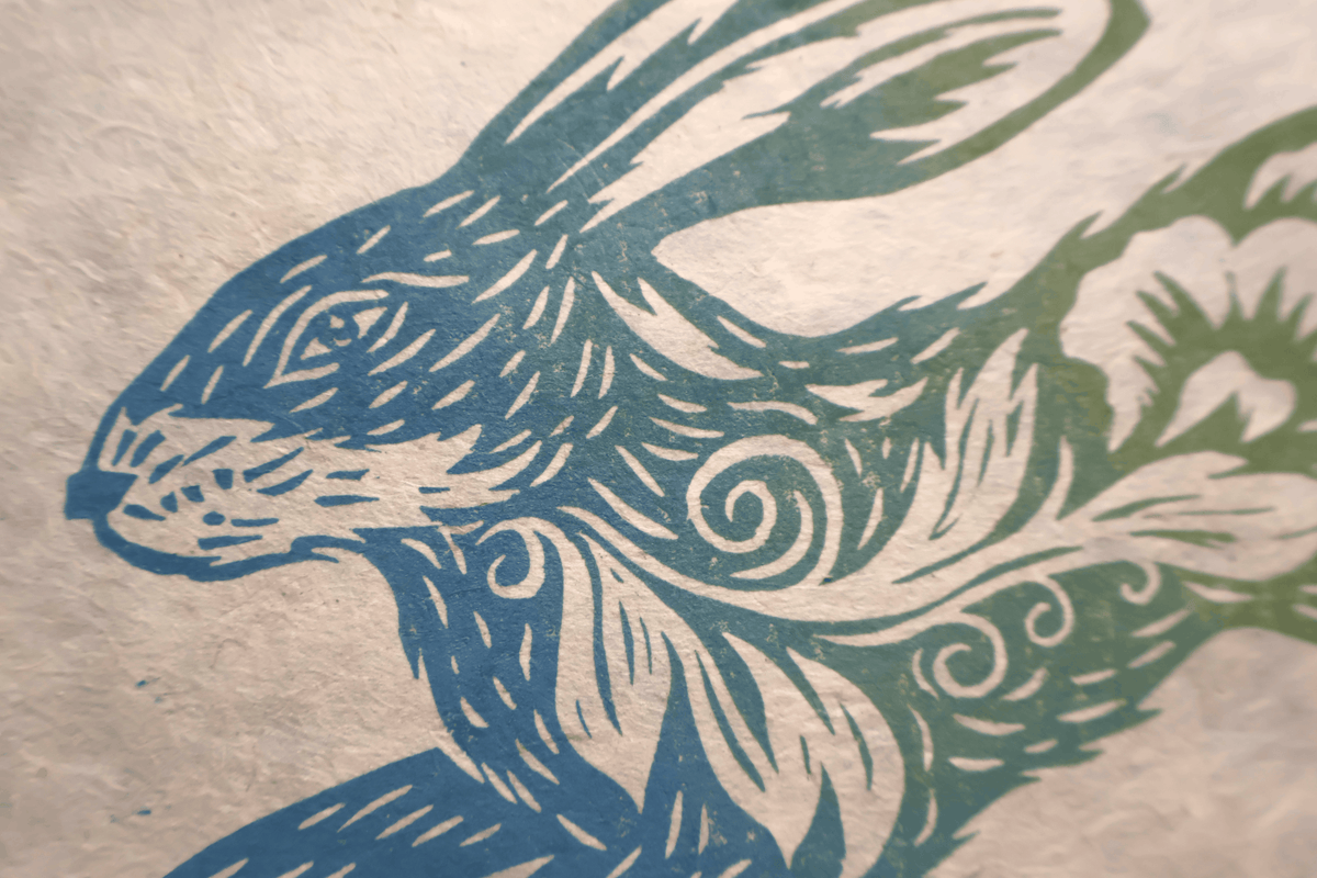 A close-up of a textured paper print featuring a stylized rabbit illustration in blue and green ink.