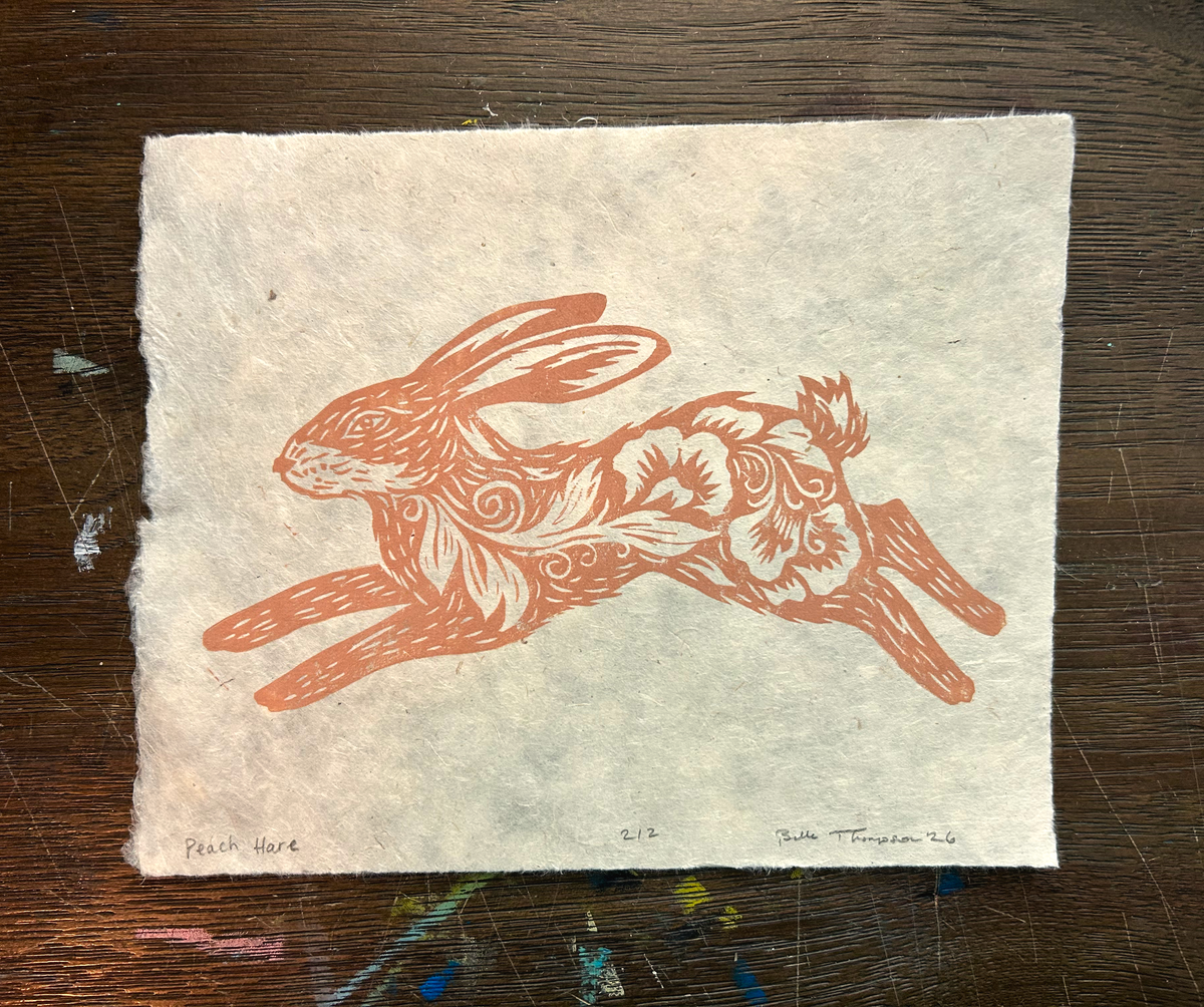 A rectangle piece of textured handmade paper featuring a printed rabbit illustration in terracotta orange on a warm off-white background, placed on a dark wooden surface.