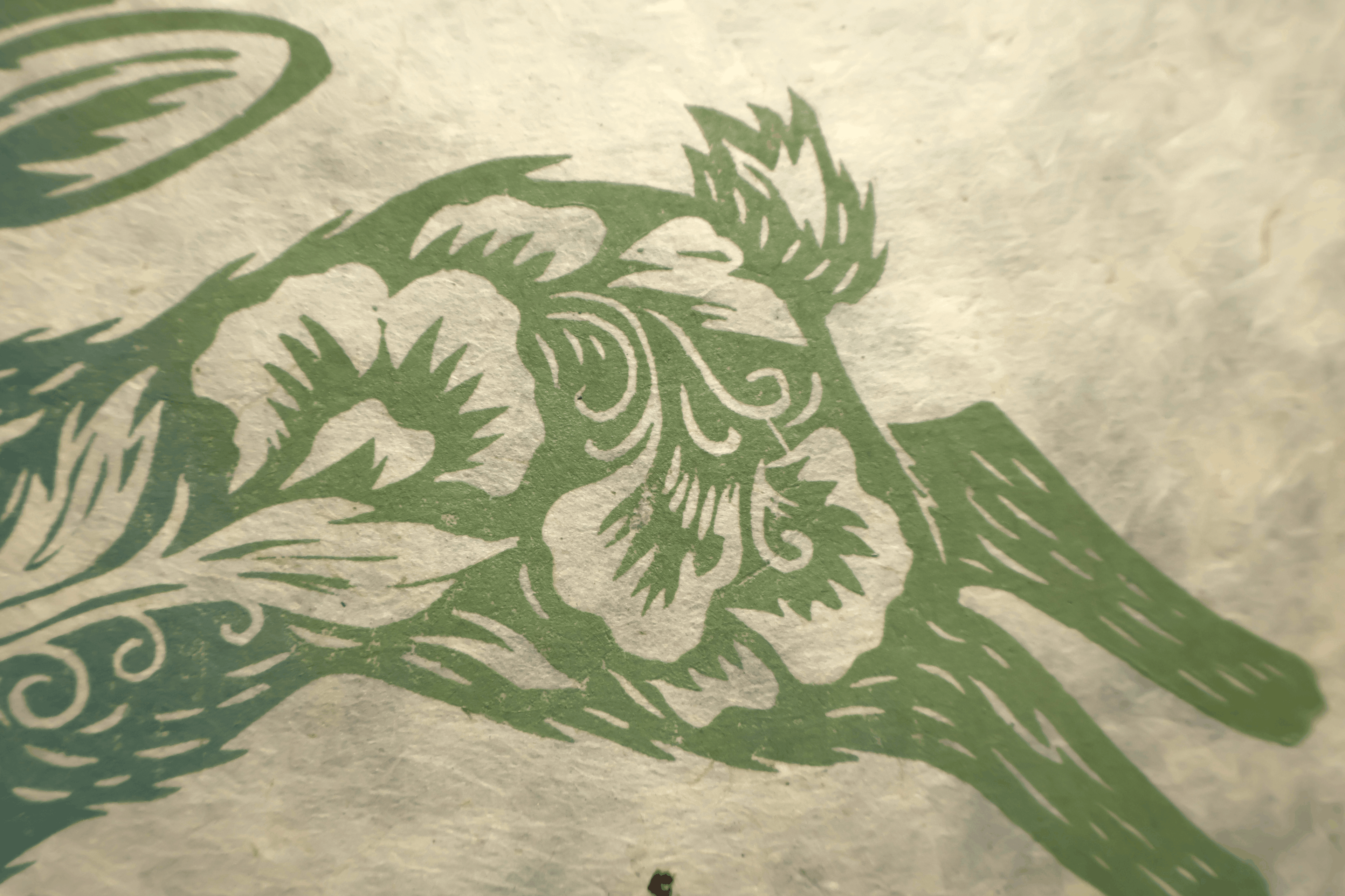 A close-up of a green floral and scroll pattern printed on textured off-white paper.