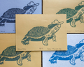 western turtle with cowboy hat and spur in the colors green on brown and blue on blue handmade linocut print signed by artist on a textured brown background