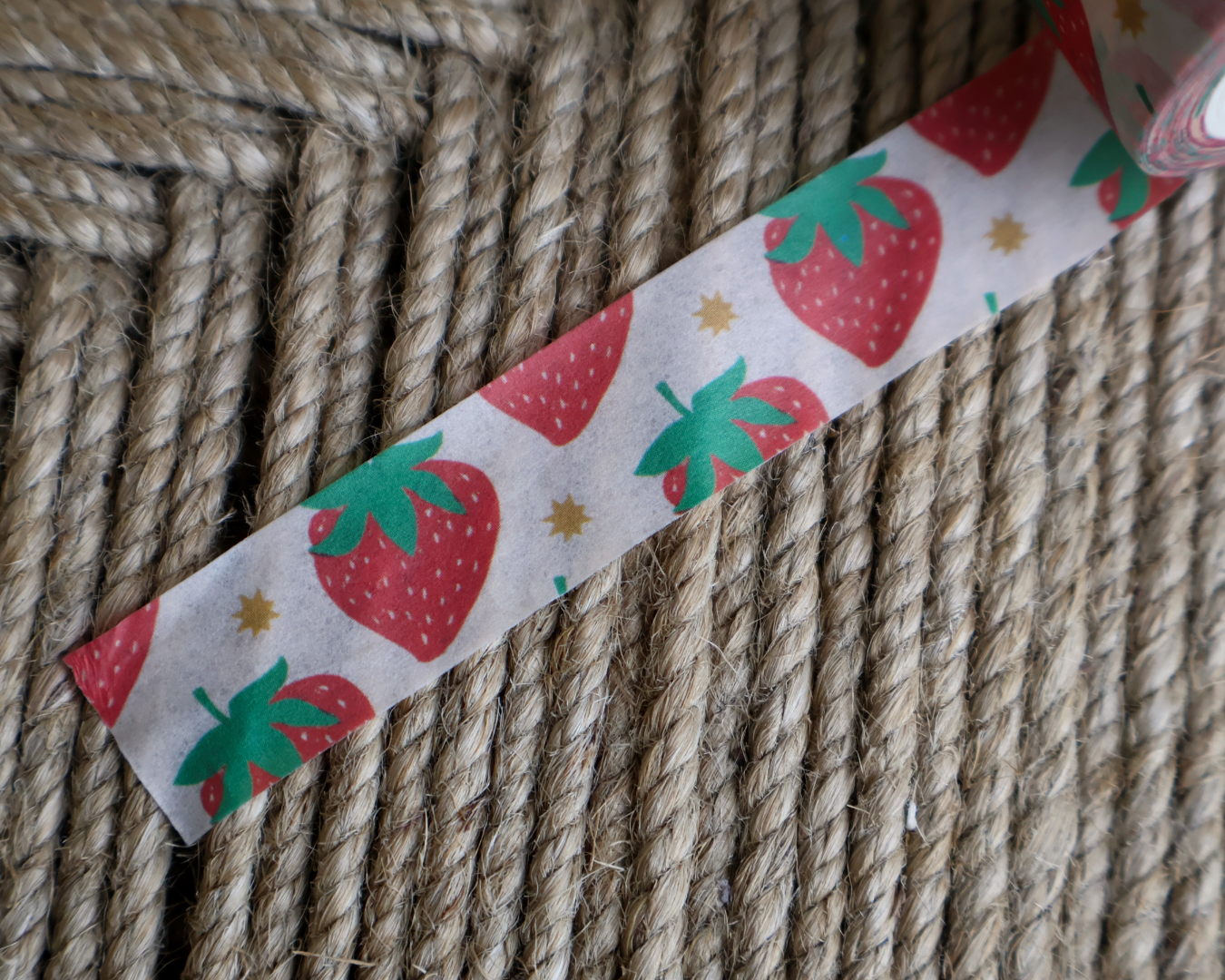 linocut design of red strawberries with gold stars on decorative washi tape. unrolled showing the design on a textured brown background. by dovetail studio