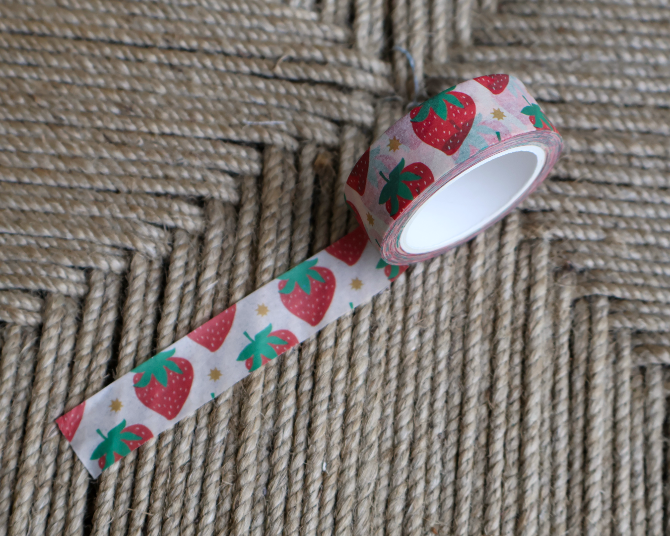 linocut design of red strawberries with gold stars on decorative washi tape. unrolled showing the design on a textured brown background. by dovetail studio