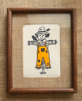 A handmade art print featuring a whimsical hand-drawn scarecrow on textured off-white paper, placed on a brown woven straw mat. The print is signed 'Patches'