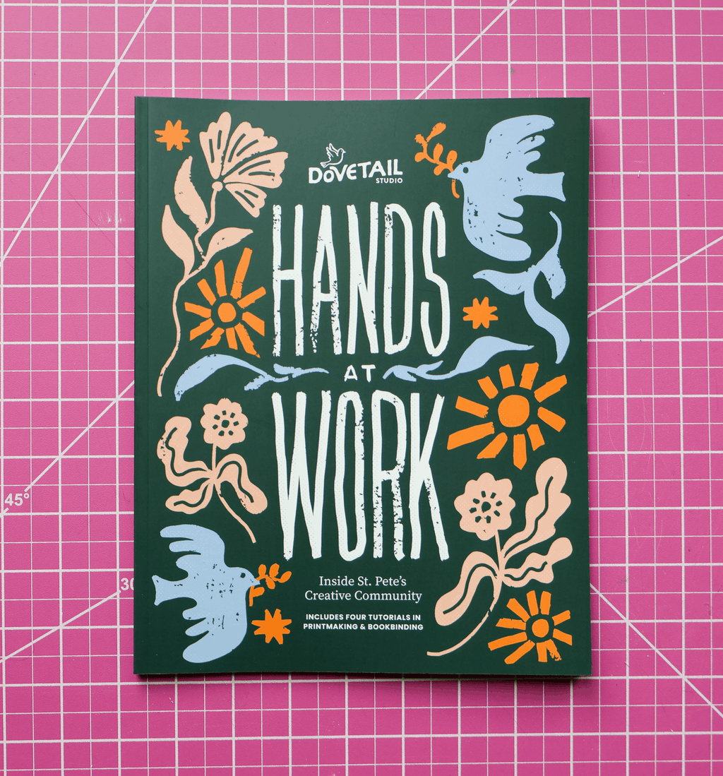 publication named hands at work inside st petersburg florida creative community including tutorials for linocut printmaking and bookbinding cover featuring flowers, stars, suns, and doves with the colors orange, blue, tan on a pink grid background by dovetail studio