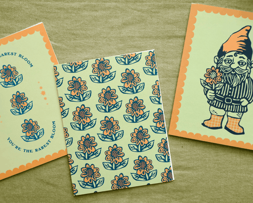 Three greeting cards with floral patterns and a gnome illustration on a textured green surface.