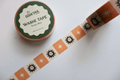 A roll of decorative washi tape with a retro pattern of orange suns and white stars on a cream background, shown next to its green and white label by Dovetail Paper.