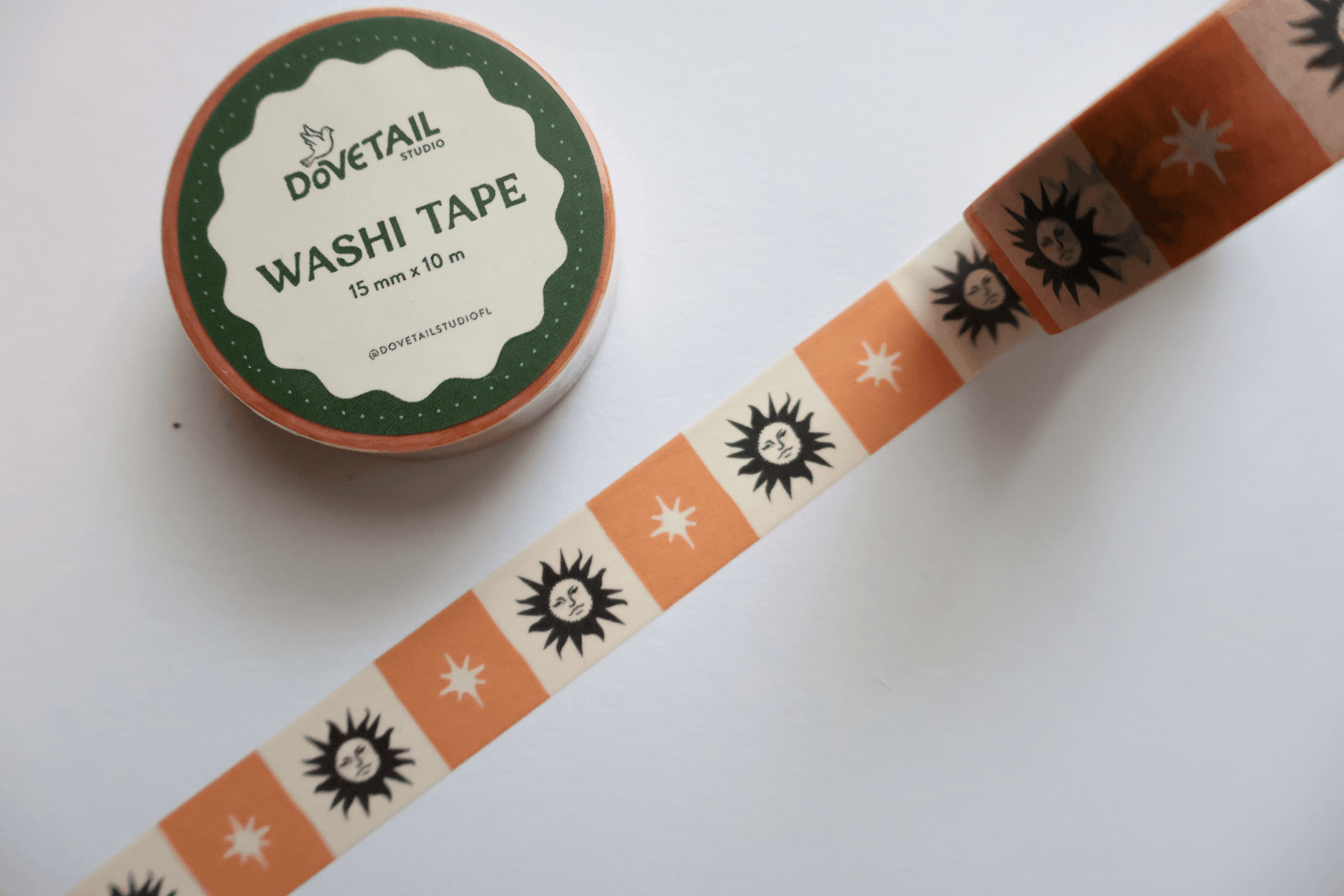 A roll of decorative washi tape with a retro pattern of orange suns and white stars on a cream background, shown next to its green and white label by Dovetail Paper.