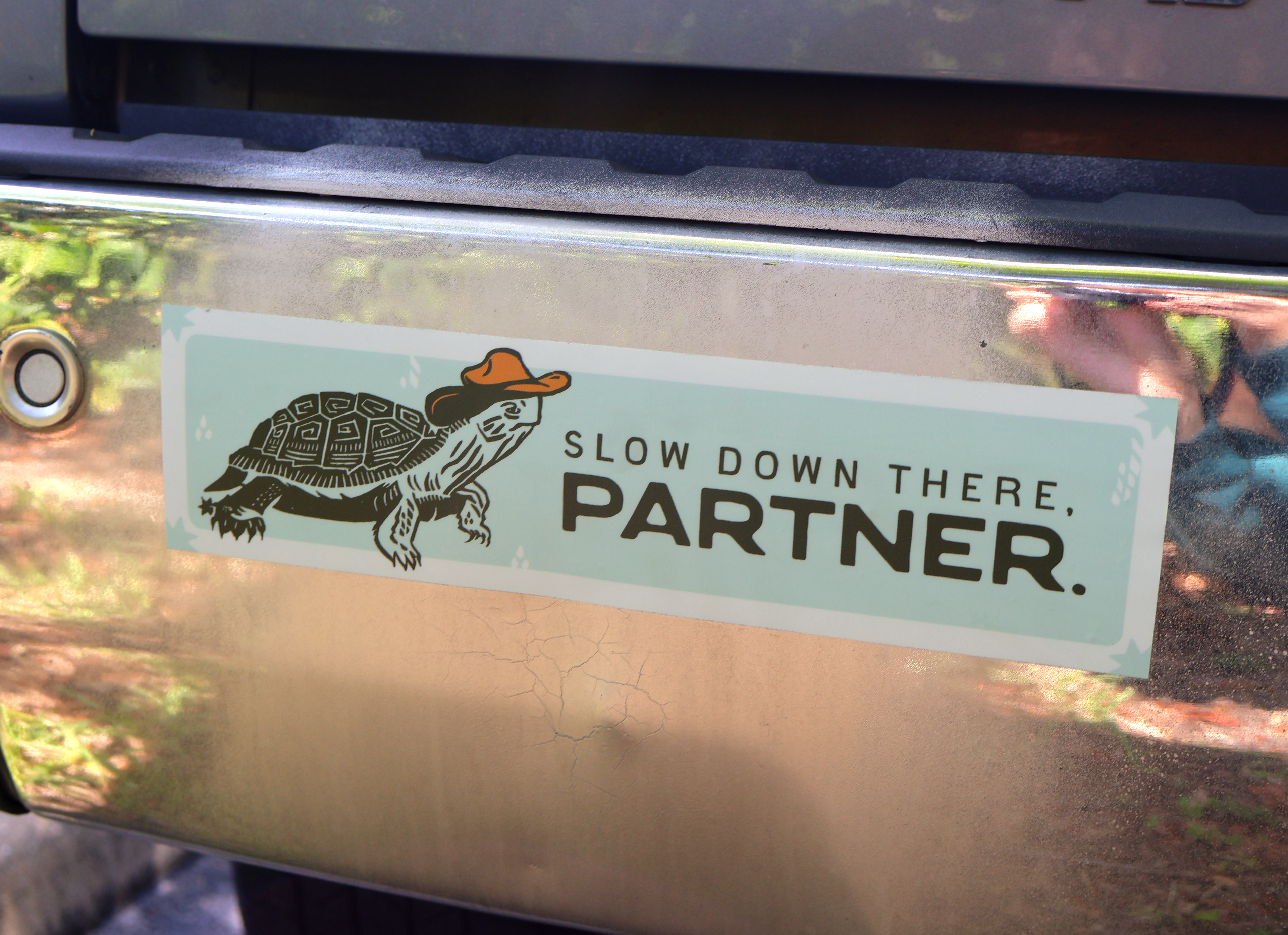 vinyl bumper sticker with a turtle wearing a cowboy hat and text 'Slow down there, partner' on truck bumper