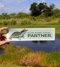 vinyl bumper sticker with a turtle wearing a cowboy hat and text 'Slow down there, partner' on a textured brown background